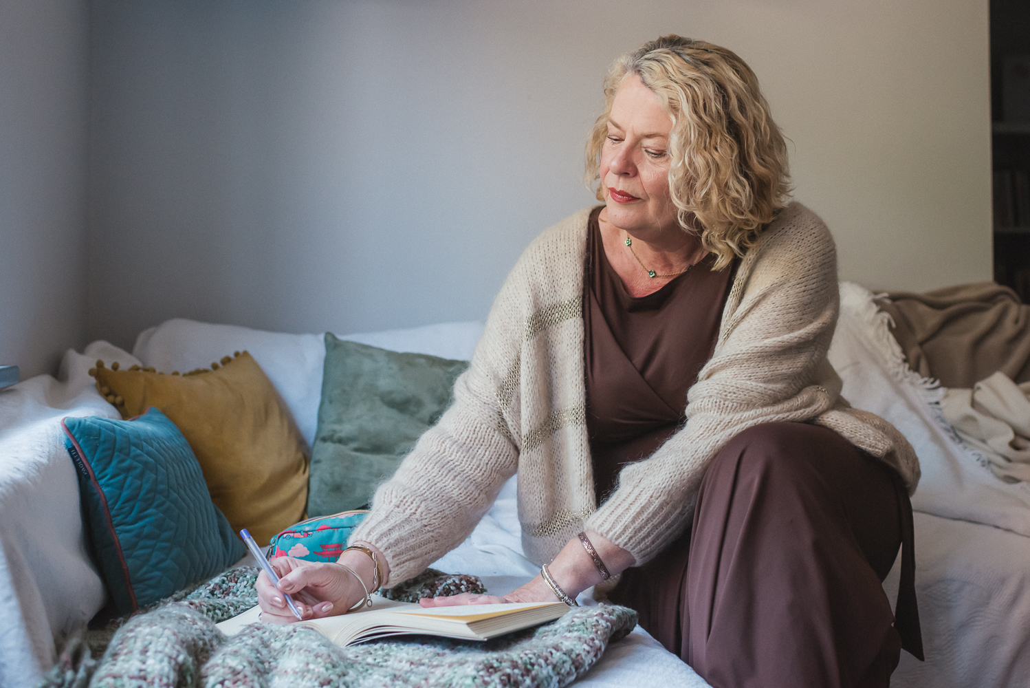 Vicky Paine writing in a journal, seated on a sofa